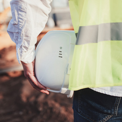 Gros plan sur un casque de chantier tenu par un homme qui porte un gilet jaune de sécurité