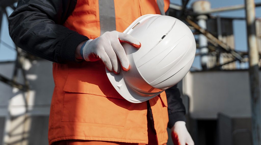 Un homme en tenue de chantier tient son casque à la main et porte des gants de sécurité
