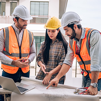 3 personnes en vêtement de chantier argumentent sur un plan d'architecte et un ordinateur