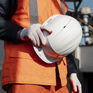 Un homme en tenue de chantier tient son casque à la main et porte des gants de sécurité