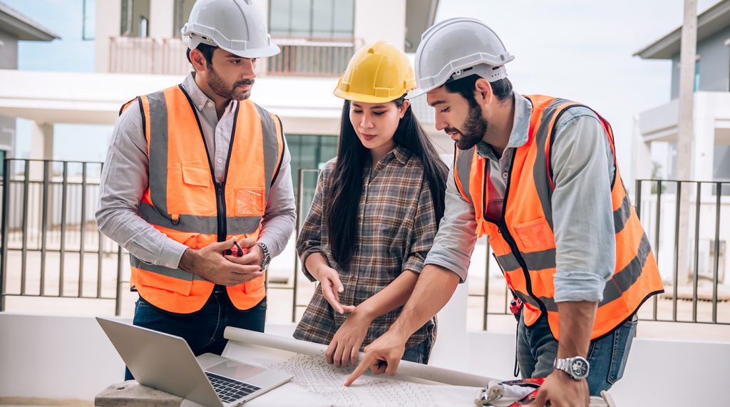 3 personnes portant des vêtement de travail chantier discutent et argumentent sur un plan d'architecte