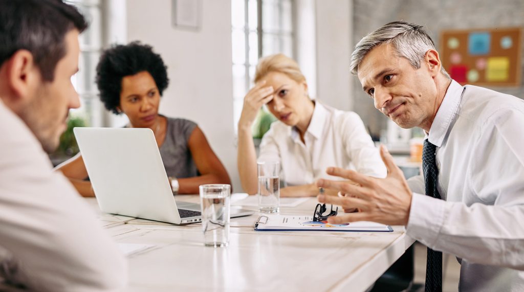 Un homme en costume discute stratégie autour d'une table de 4 collaborateurs.